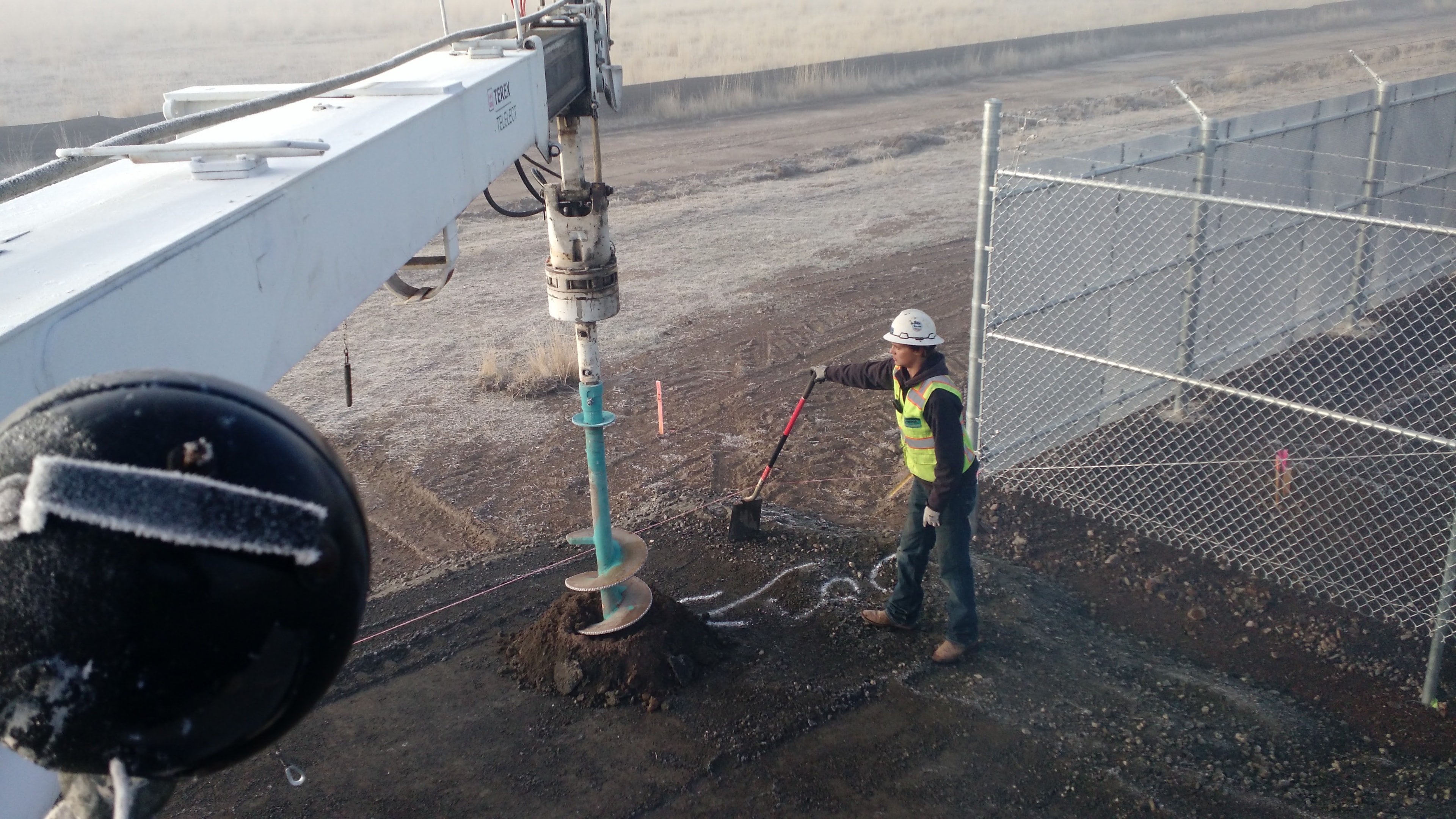Superior Fence crew drilling post holes with auger equipment at an industrial chain link project