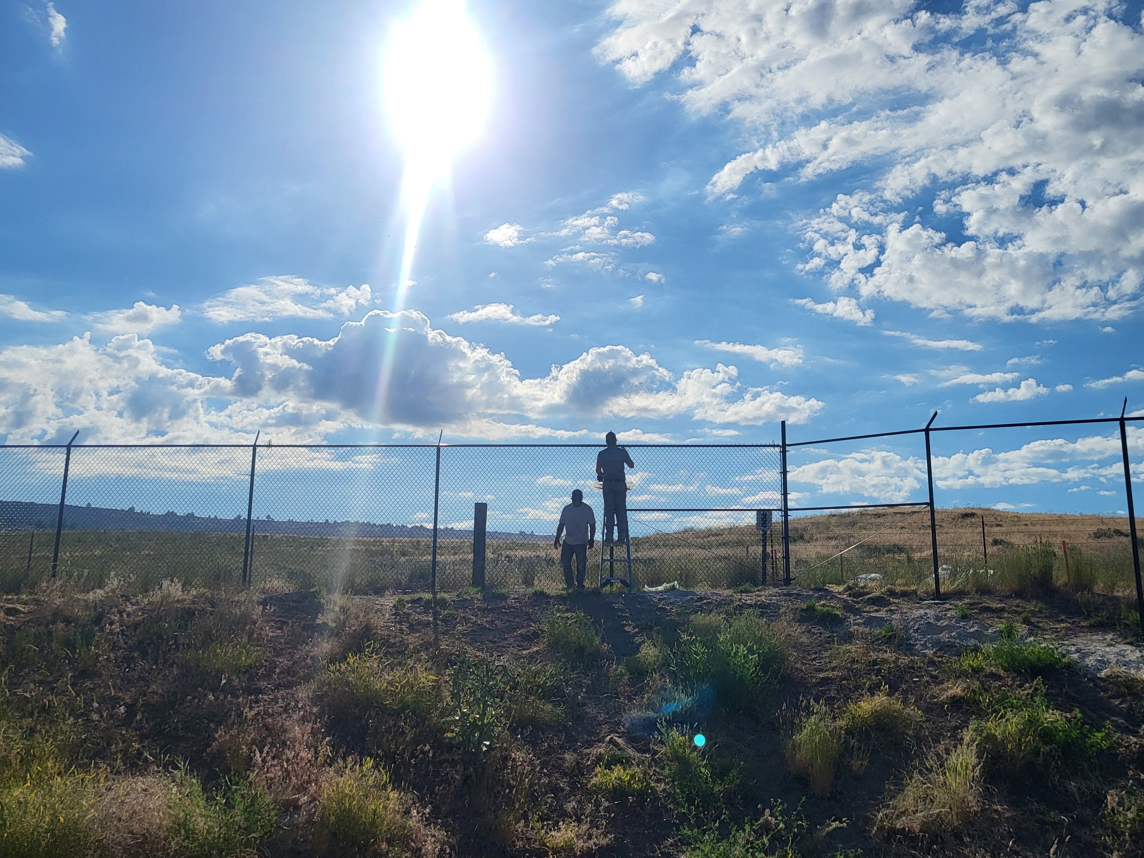 Superior Fence crew installing chain link fence on a rural hilltop under a dramatic blue sky