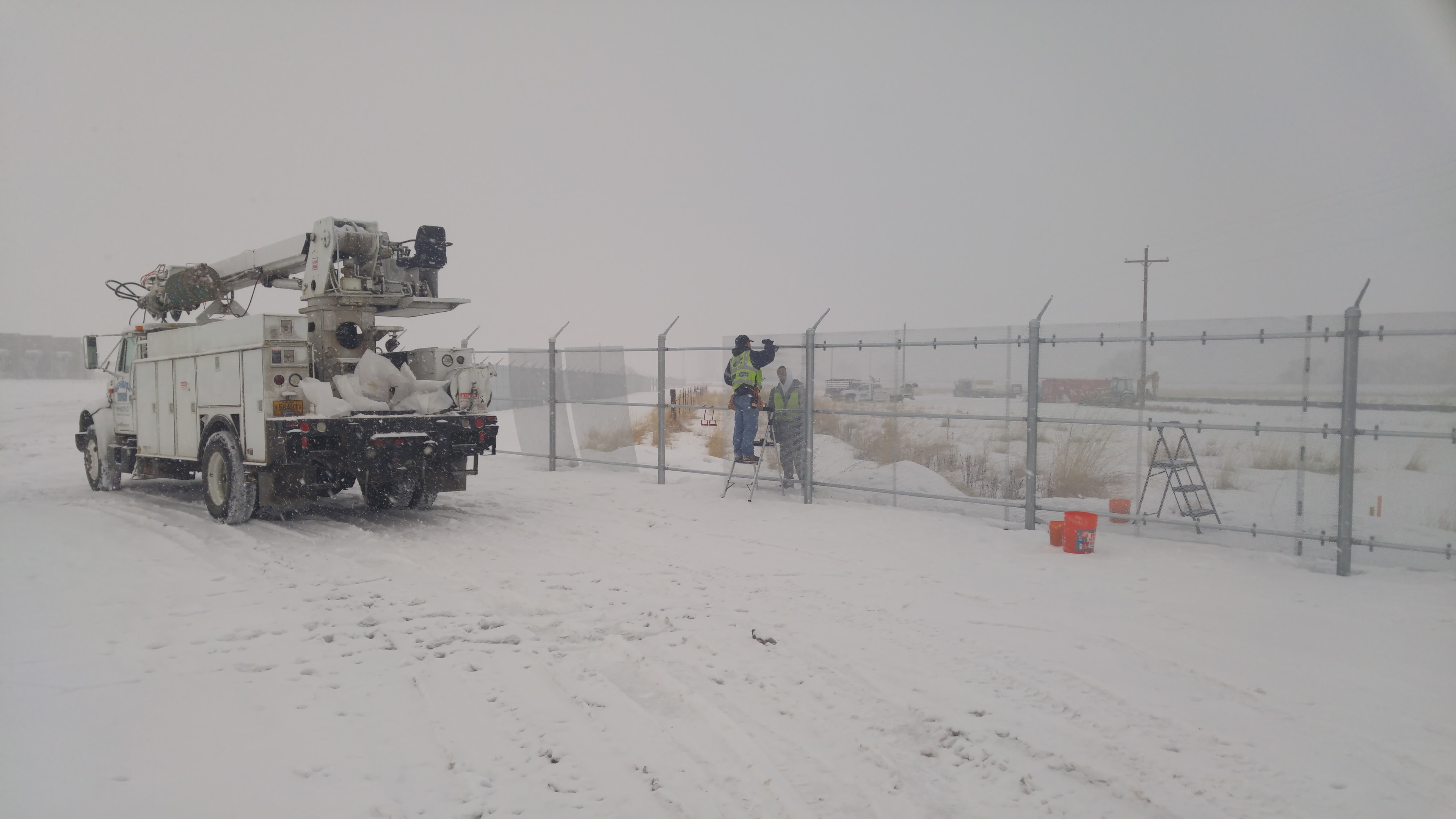 Superior Fence crew installing industrial security fence in heavy snow conditions