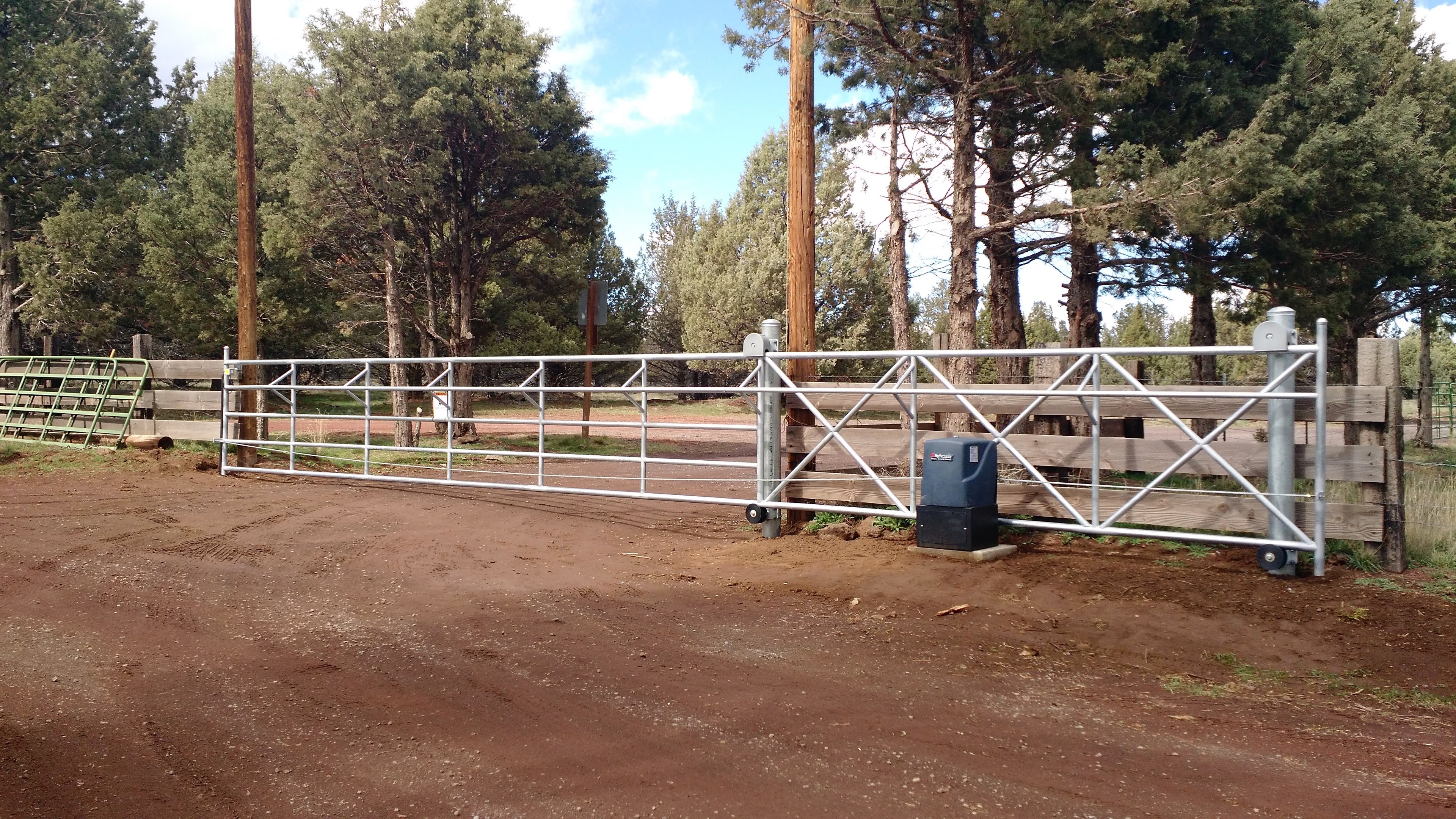 Custom galvanized ranch gate with automated operator on a dirt driveway
